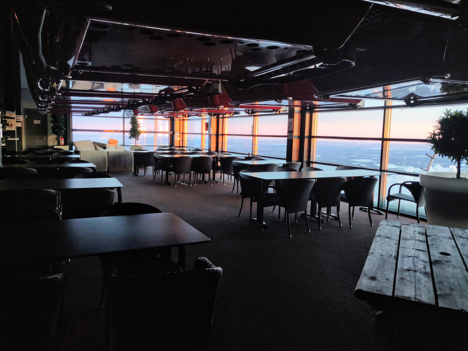 Gondola cable cars hanging on restaurant Gondol premises, tables are under them and sun is shining from large windows.